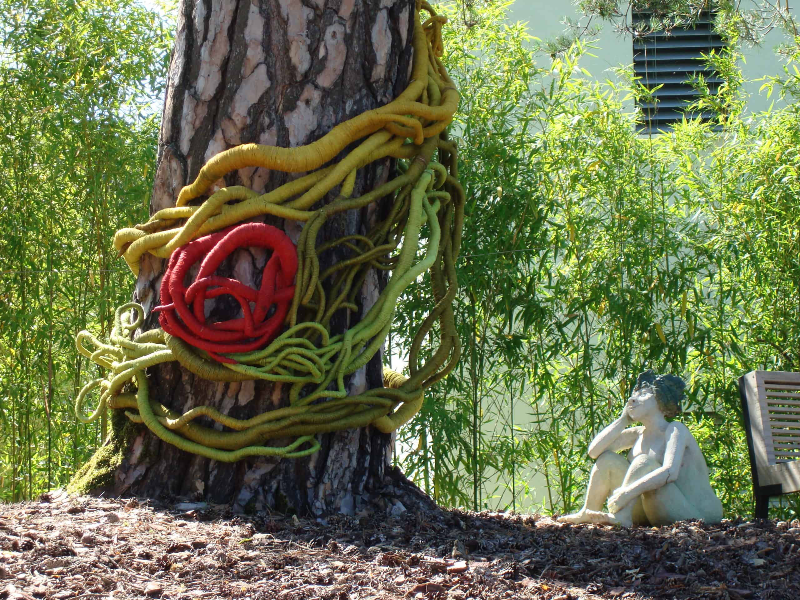 giant red green and yellow sculptures wrapped around a tree by Aude Franjou