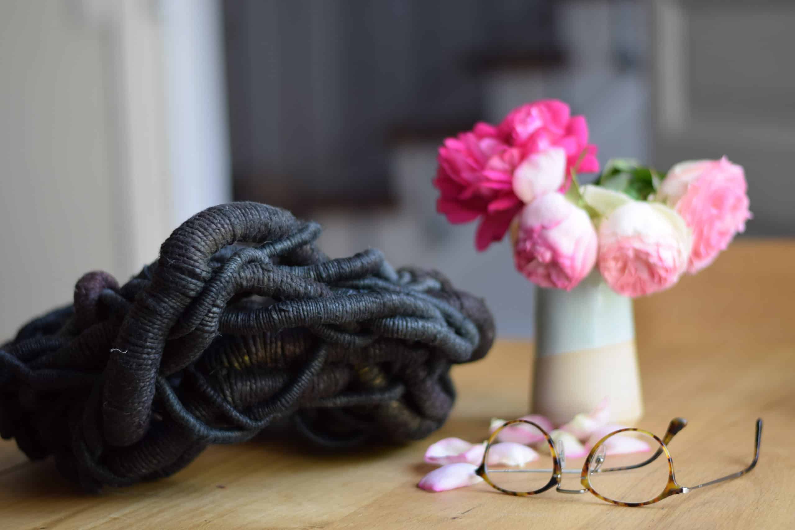 Picture of a black sculpture next to a vase with flowers and a pair of glasses.