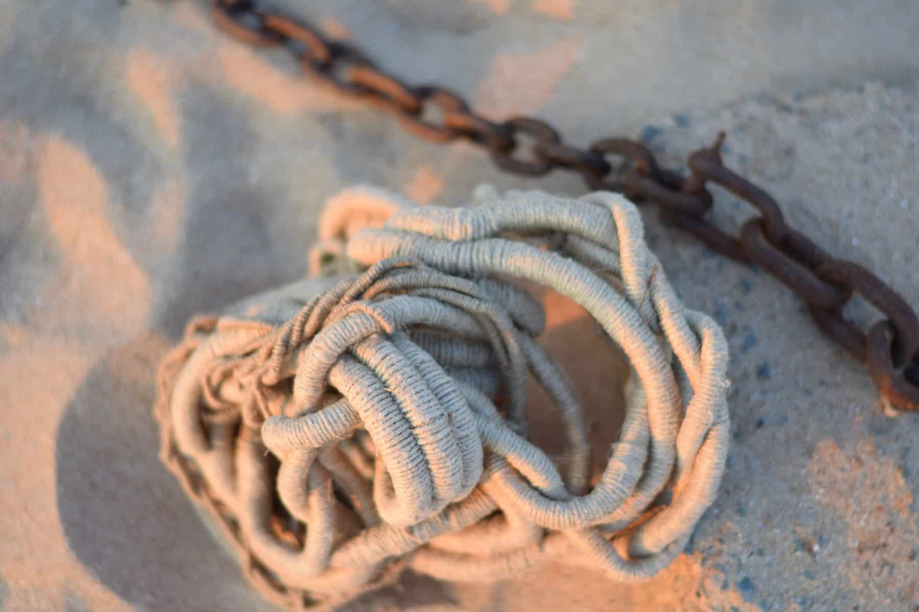 coral-like white sculpture by Aude Franjou in beach sand next to rusty iron chain