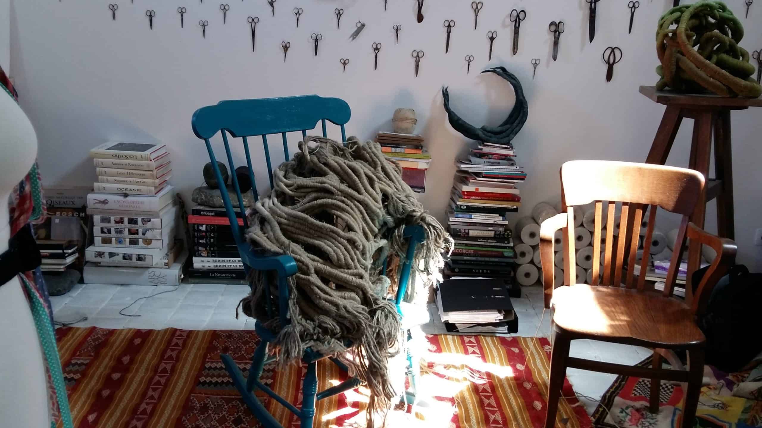 Picture of artist Aude Franjou's workshop depicting a rocking chair with a sculpture on it, and a collection of scissors on the walls.