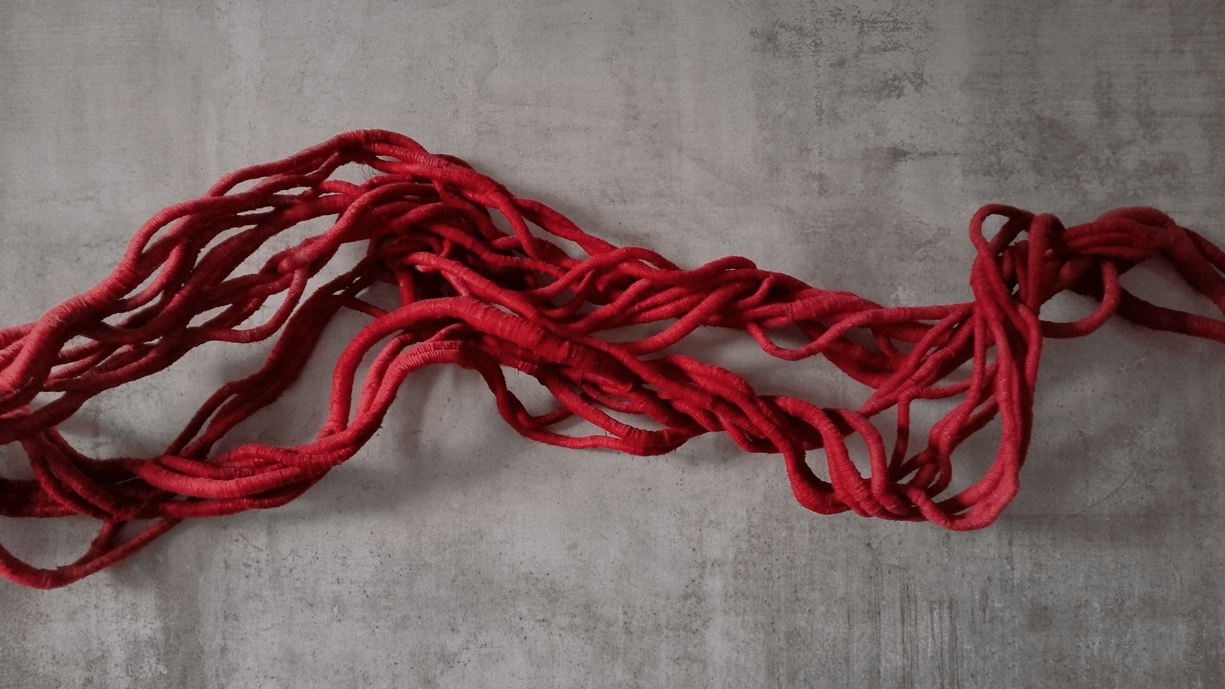A blood red linen sculpture on a smooth concrete wall by sculptor Aude Franjou