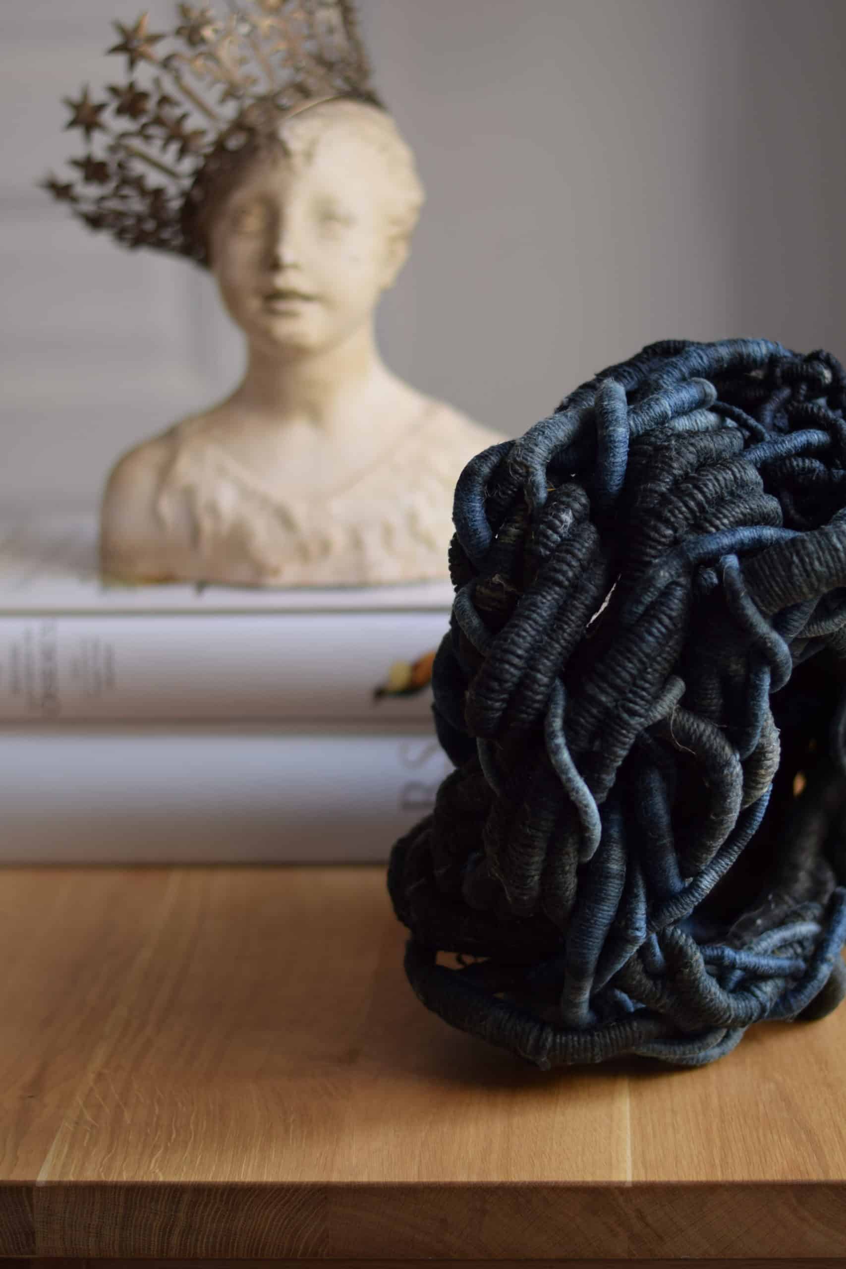 Picture of a dark blue sculpture on a table by artist Aude Franjou. In the background a stone bust is wearing a crown.