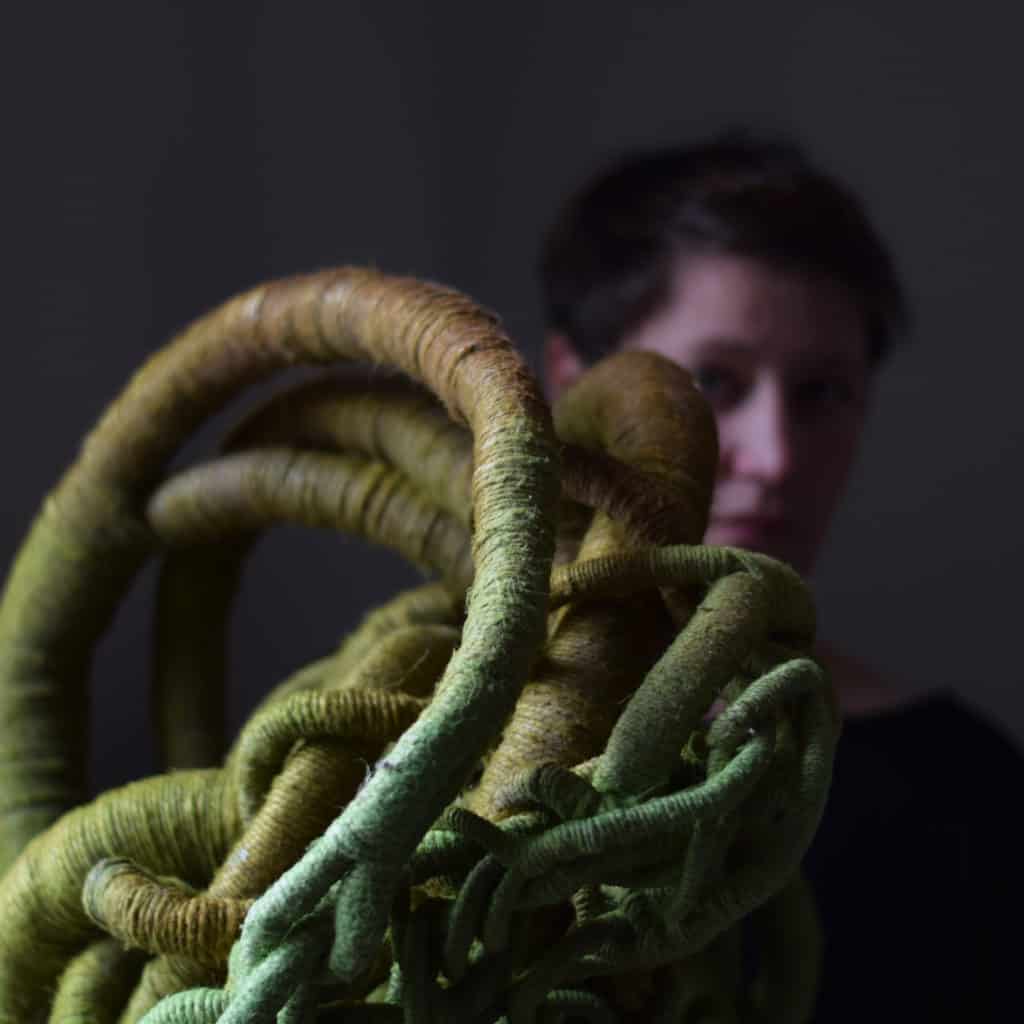 Picture of artist Aude Franjou standing behind a green sculpture