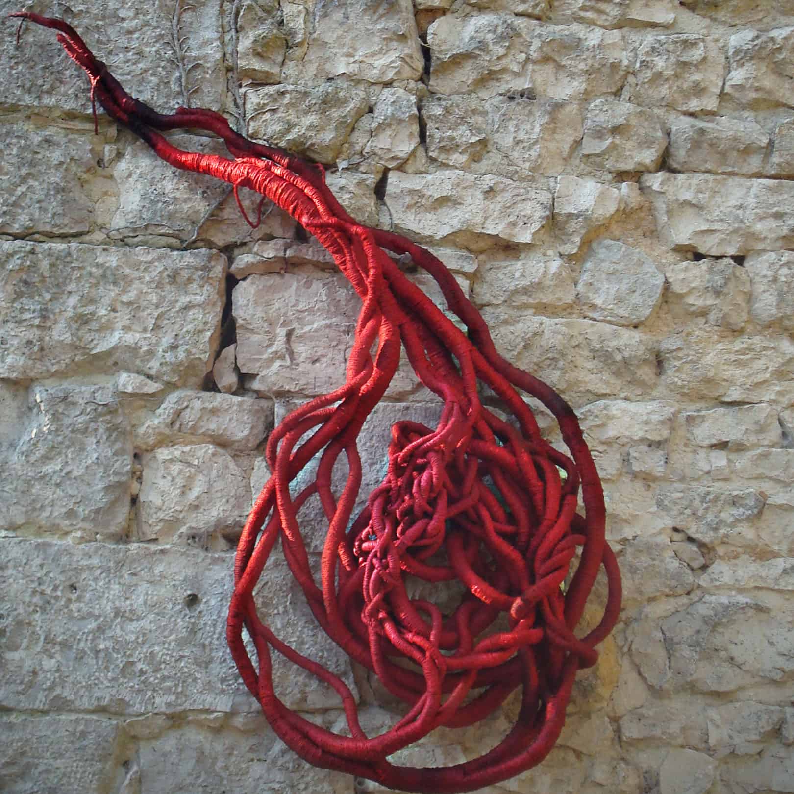 red linen sculpture in the shape of a comma hanging on a stone wall